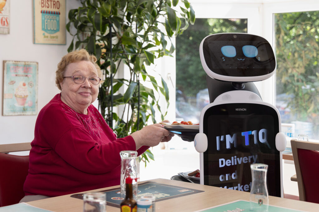 Eine Bewohnerin greift nach einem Tablett von einem Service-Roboter.
