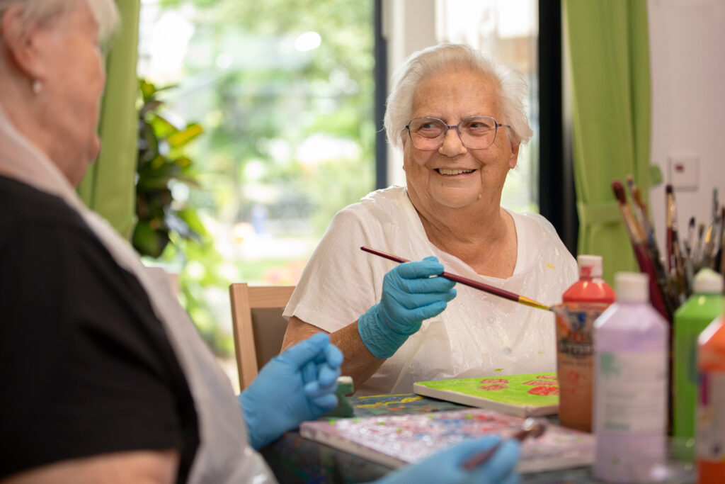 Eine Bewohnerin, die an der Kreativgruppe teilnimmt, lächelt in die Kamera.