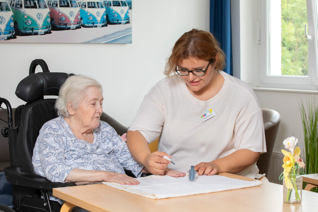 Eine Mitarbeiterin lackiert einer Bewohnerin die Fingernägel