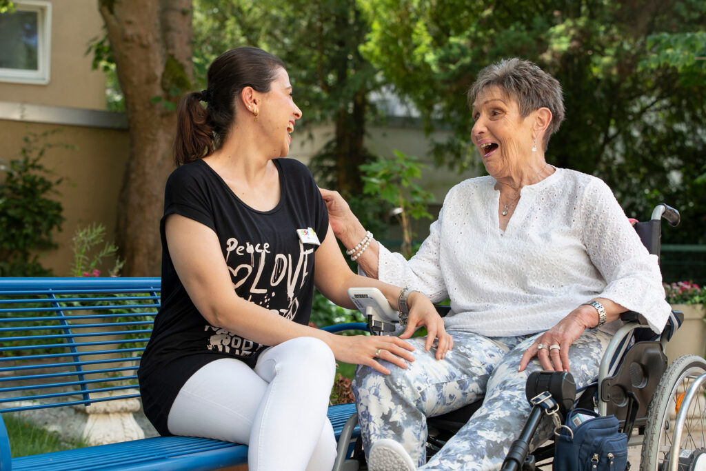 Eine Mitarbeiterin und eine Bewohnerin sind im Gespräch und lachen herzlich.