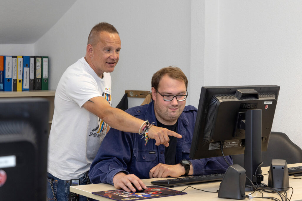 Ein Mitarbeiter erläutert einem Teilnehmer einen Arbeitsschritt am Computer.
