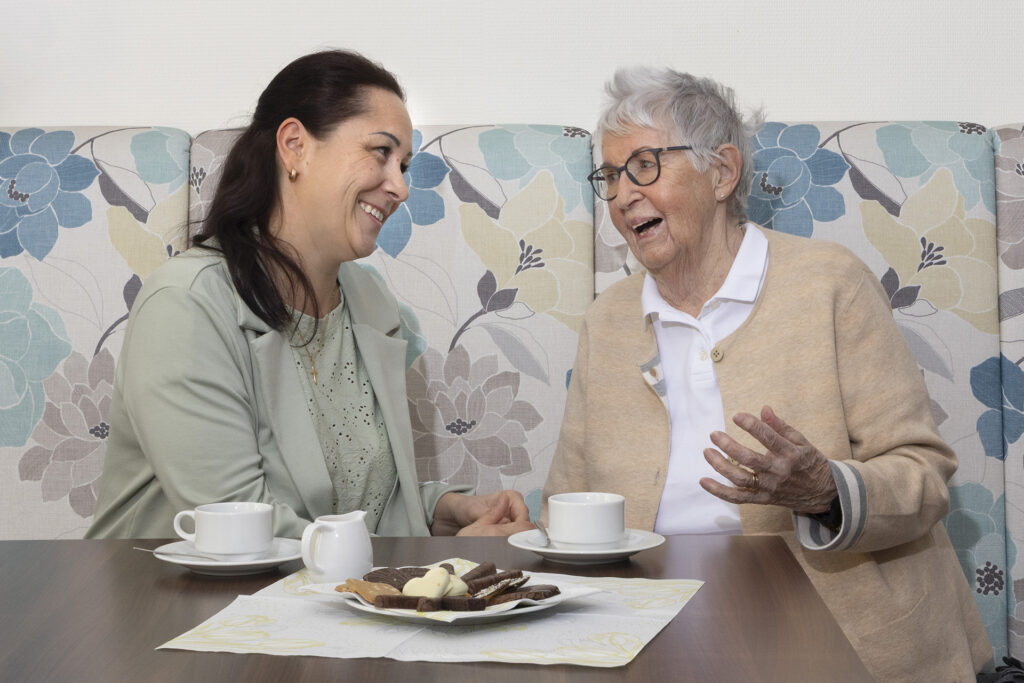 Eine Mitarbeiterin ist mit einer Seniorin bei einer Tasse Kaffee im Gespräch.