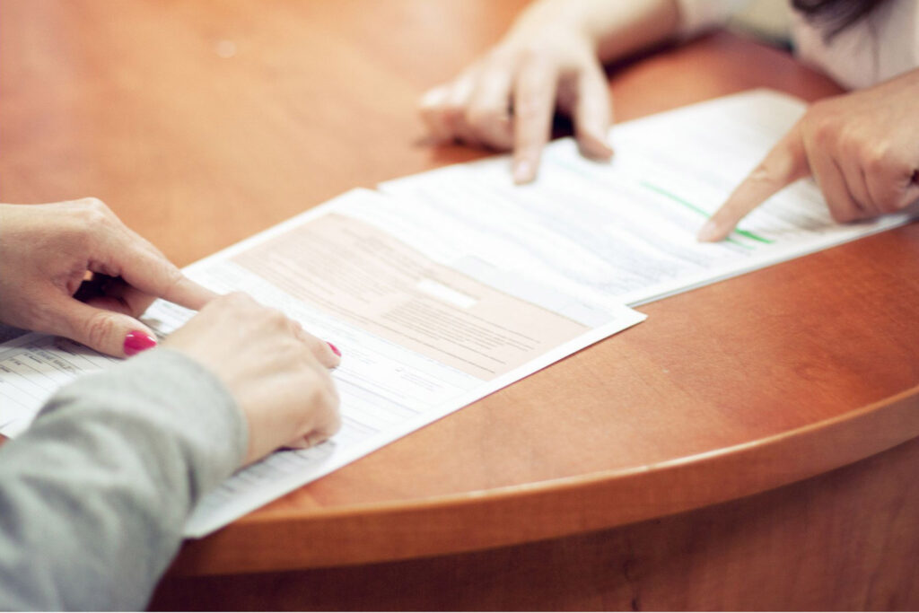 Hände von zwei Personen auf verschiedenen Formularen, die bearbeitet werden.