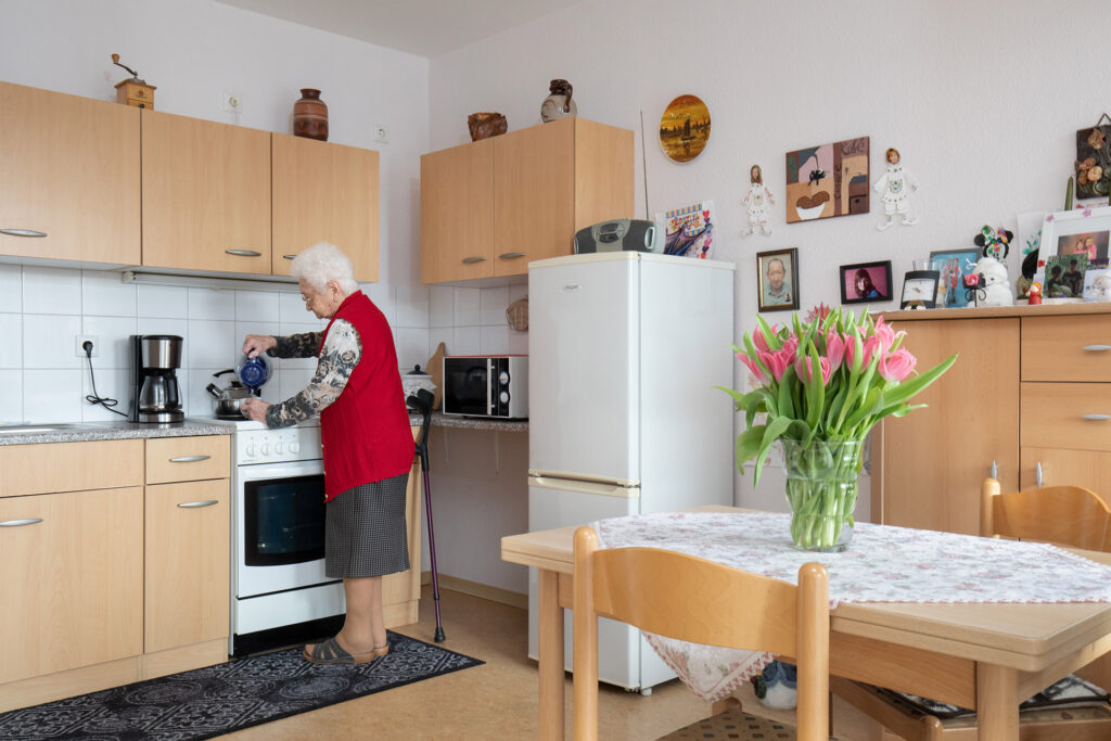 Blick in einen Küchen- und Essbereich in einer Wohnung im Peter Reise-Haus. Eine Bewohnerin gießt sich gerade Tee in einen Becher.