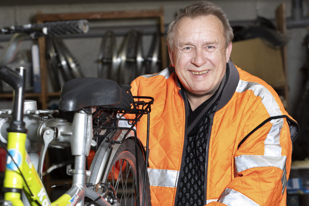 Ein Mitarbeiter in Dienstkleidung repariert ein Fahrrad und lächelt in die Kamera.