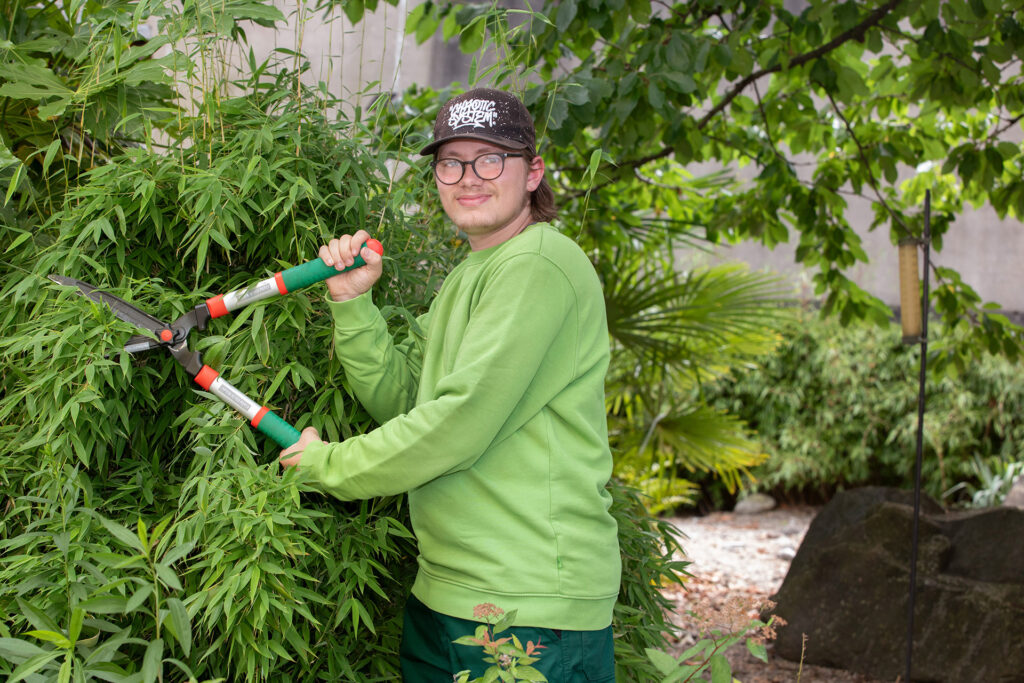 Ein Teilnehmer schneidet mit einer großen Heckenschere eine Hecke.